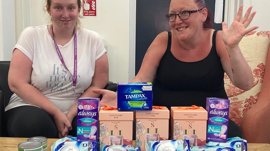 Sanctuary residents sat smiling with numerous sanitary products in front of them on a table