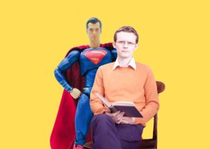 An image of Neil, a man sat wearing an orange jumper holding a book in front of a Superman figure.