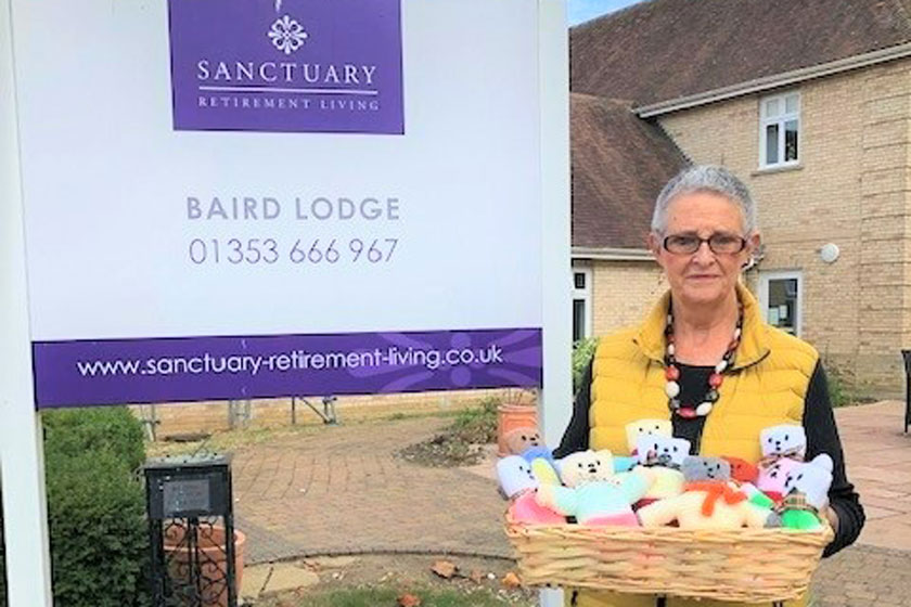 Sanctuary staff member standing outside Baird Lodge with a basket of knitted teddies