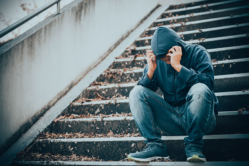Stock image of a young man sitting on some steps holding his head in his hands