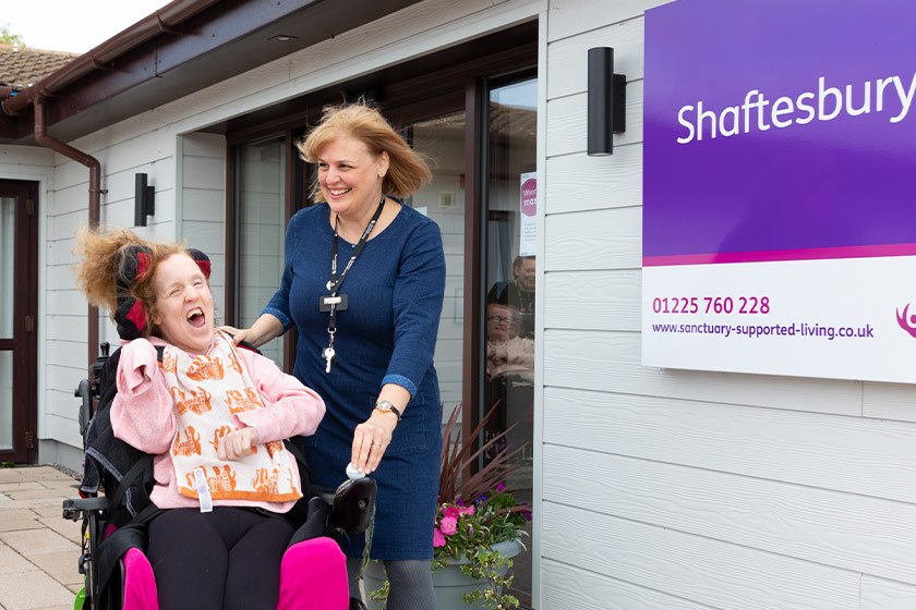 Smiling staff member and resident, who is a wheelchair user, outside of the Shaftesbury Court main entrance