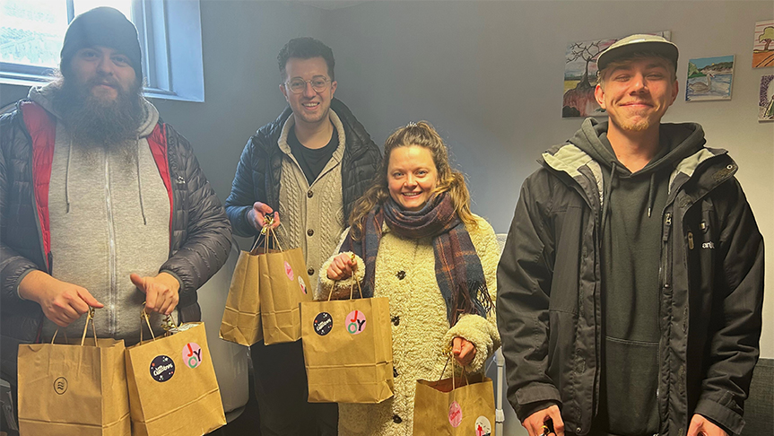 Residents and staff with bags Three men and one woman stood holding brown paper gift bags, smiling at the camera