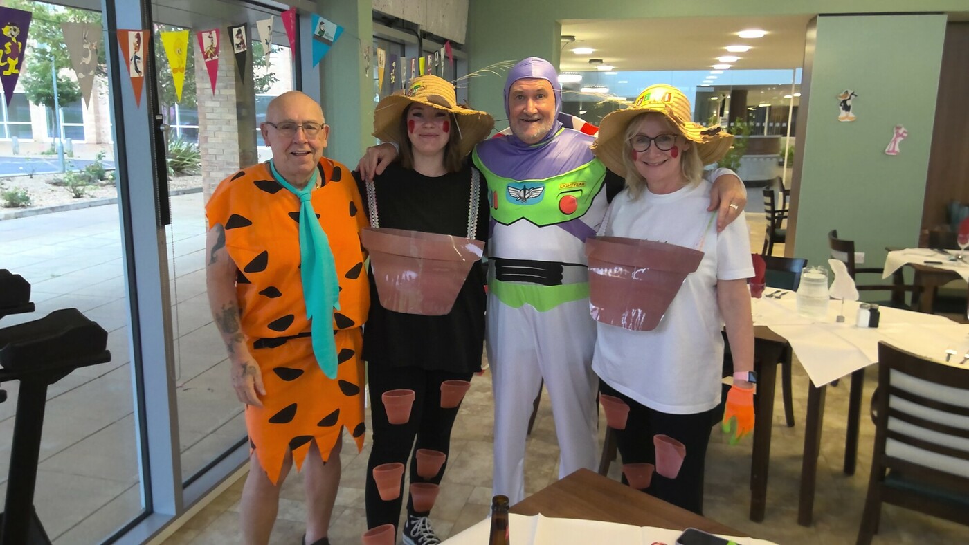 Two women and two older men all dressed up, stood together and smiling at the camera. One man is Fred Flintstone, the other is Buzz Lightyear and the two women are Bill and Ben the Flowerpot Men.