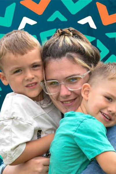 A young woman with glasses is smiling and hugging two young boys, one on each side