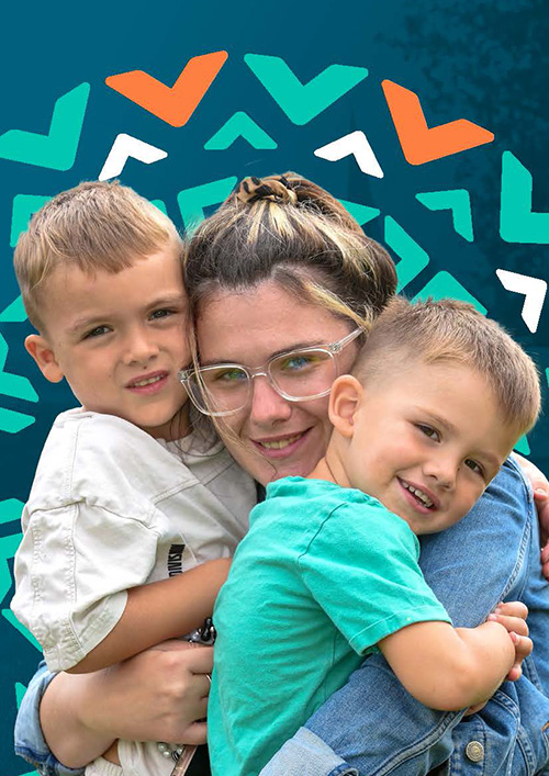 A young woman with glasses is smiling and hugging two young boys, one on each side