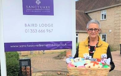 Lynda standing outside Baird Lodge with a basket of knitted teddies