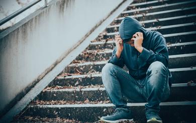 Stock image of a young man sitting on some steps holding his head in his hands