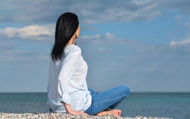 Stock image of a woman sitting on a pebble beach looking out to sea
