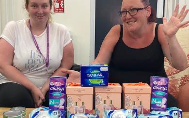 Linsey and Kerry sat smiling with numerous sanitary products in front of them on a table