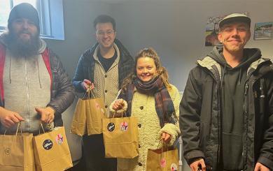 Three men and one woman stood holding brown paper gift bags, smiling at the camera