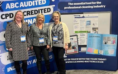 Three women wearing patterned tops and lanyards pose for a photograph in front of a board that reads "Cleaning matters"