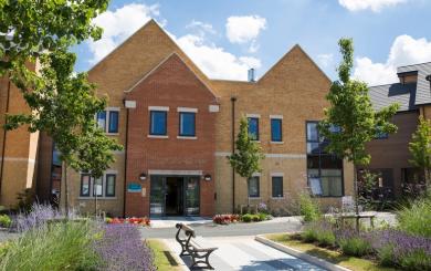 Exterior image of Noble House, a modern building with large windows and a beautiful garden with lucious green grass, trees and colourful flowers