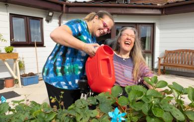 SSL staff member and resident in the garden on a sunny day watering plants with a watering can