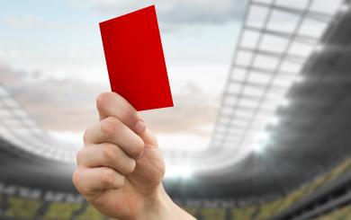 A hand holding up a red card in a stadium