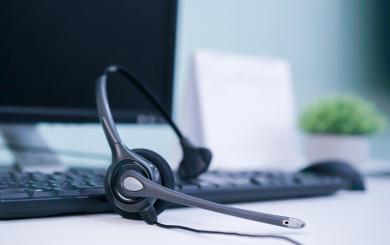 Close up of a telephone headset on top of a black computer keyboard with a monitor in the background