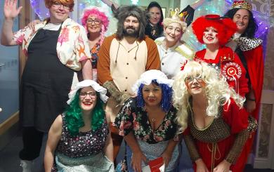A group of 10 staff members from Whitley Court and Dunboyne Court dressed as characters from the pantomime 'Smoochy and the Beast,' wearing vibrant costumes, bold makeup, and colourful, extravagant wigs.