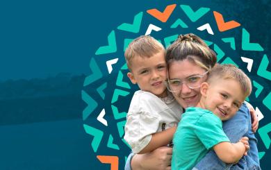 A young woman with glasses is smiling and hugging two young boys, one on each side