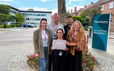 Five Sanctuary colleagues standing outside Sanctuary House holding an Investors in People Platinum accreditation plaque