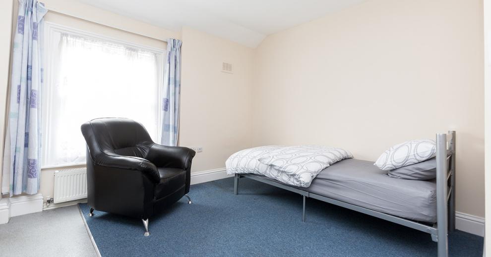 Minimalist, orderly room with a vast amount of room for a bed, armchair, and vibrant window light.