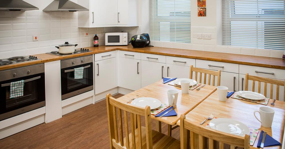 Classic kitchen. With white subway tiles and cupboards decor and wood finished work top, flooring and dining table. Alongside stylish appliances.