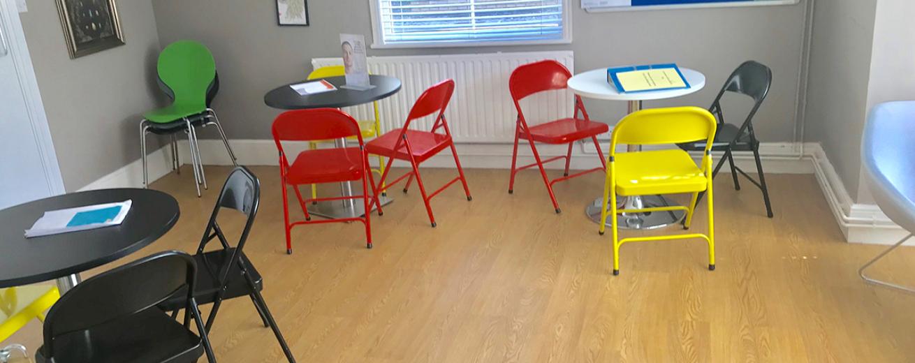 Assortment of bold coloured, metal folding chairs placed around three circular tables.