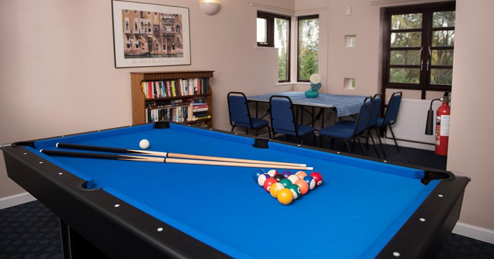 Black and blue snooker table with a corner seating area and bookshelf in the foreground.
