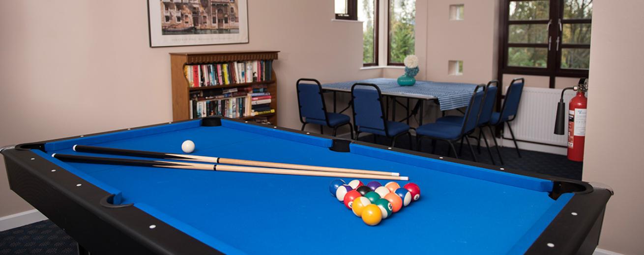 Black and blue snooker table with a corner seating area and bookshelf in the foreground.