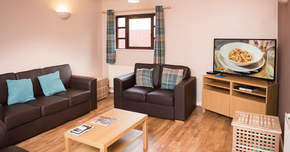 Spacious seating area with a brown leather three-piece-suite with turquoise cushions and complimentary wooden flooring a room accessories.