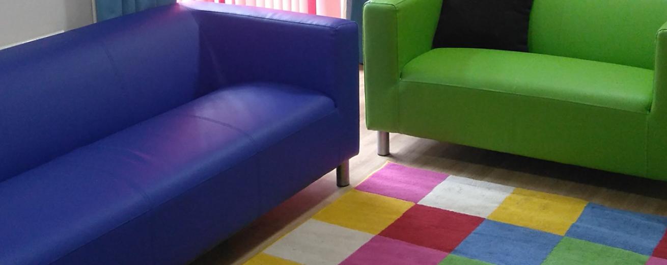 Elongated purple and lime green sofas placed around checked multicoloured rug.