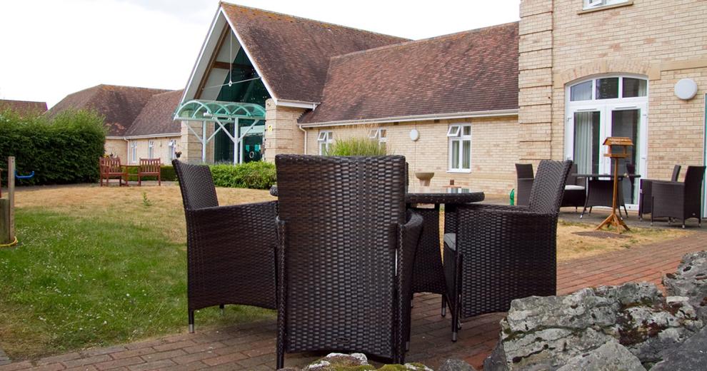 Two outdoor charcoal wicker dining sets are placed amongst the bricked walkways surrounding the grassed area.