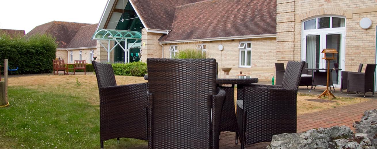 Two outdoor charcoal wicker dining sets are placed amongst the bricked walkways surrounding the grassed area.
