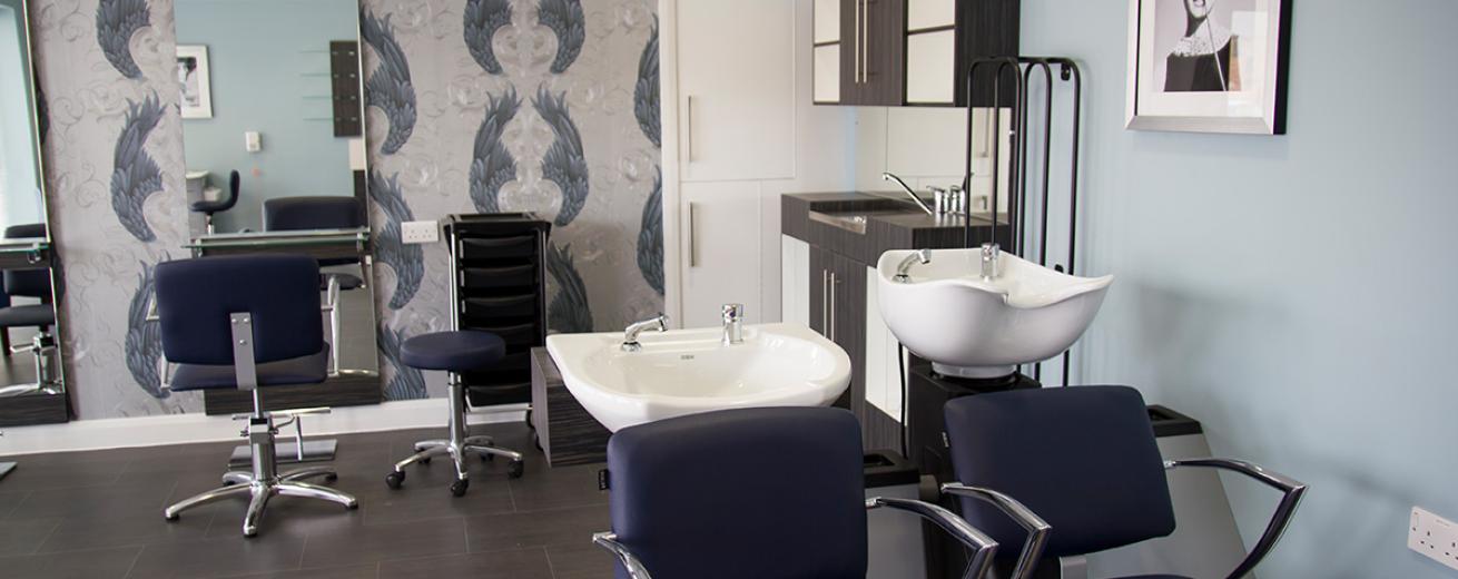 Roomy onsite hair salon, using a classic muted colour palette throughout. Navy and silver hairdressing chairs pop against the white basins or in the reflections of the large mirrors.