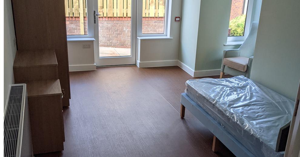 Spacious, furnished bedroom, with window seated armchair and accessibility to an outdoor area.