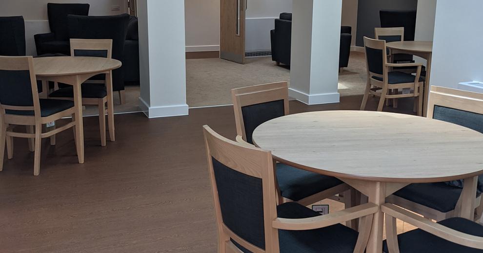 Multiple circular wood dining tables with matching wood chairs and leather cushioning.