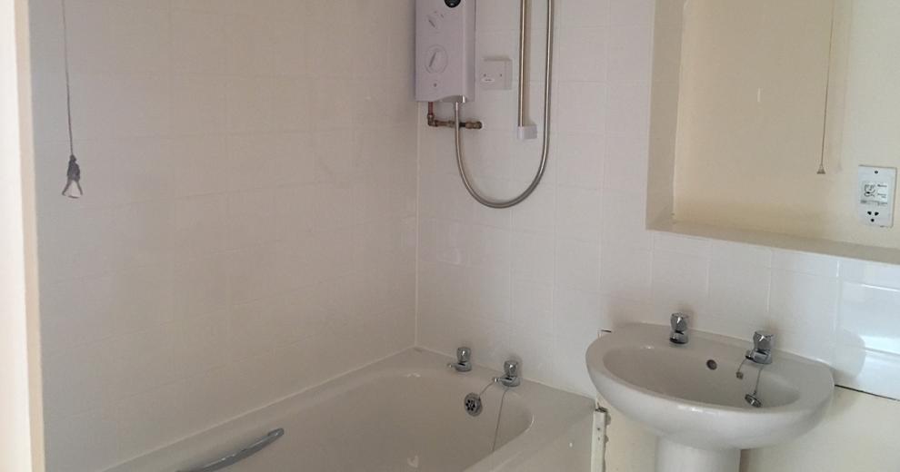 Ivory bathroom suite with silver attachments, contrasted with white square tiles and functional over bath shower.