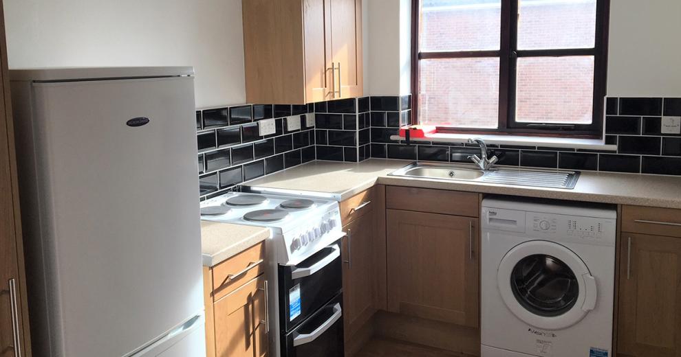 White painted decor contrasted splash-back glossy black subway tiled kitchen, with light wood styled cupboards and electrical white goods installed.