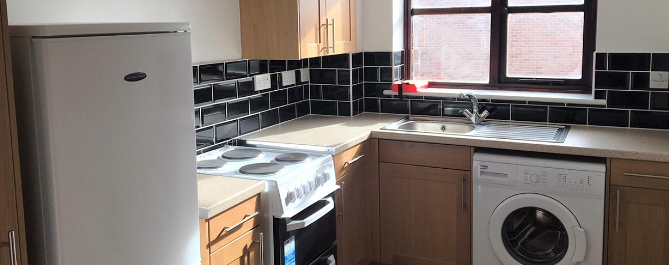 White painted decor contrasted splash-back glossy black subway tiled kitchen, with light wood styled cupboards and electrical white goods installed.