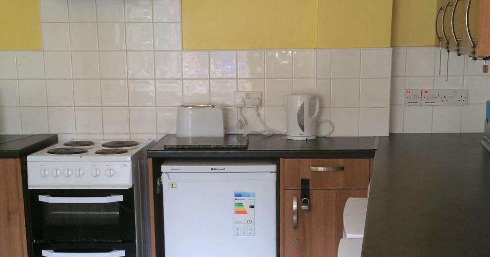 Earth toned communal kitchen with contrasting brown over head and undercounter cupboards. As well as access to white goods appliances.