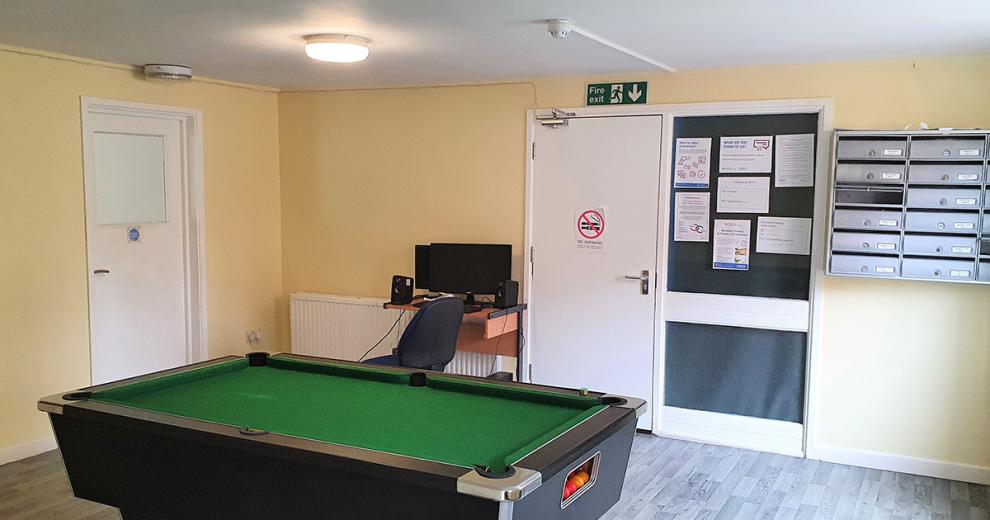 Sizeable green cloth and dark wood surround pool table, also hosting a computer set up and functional office storage.