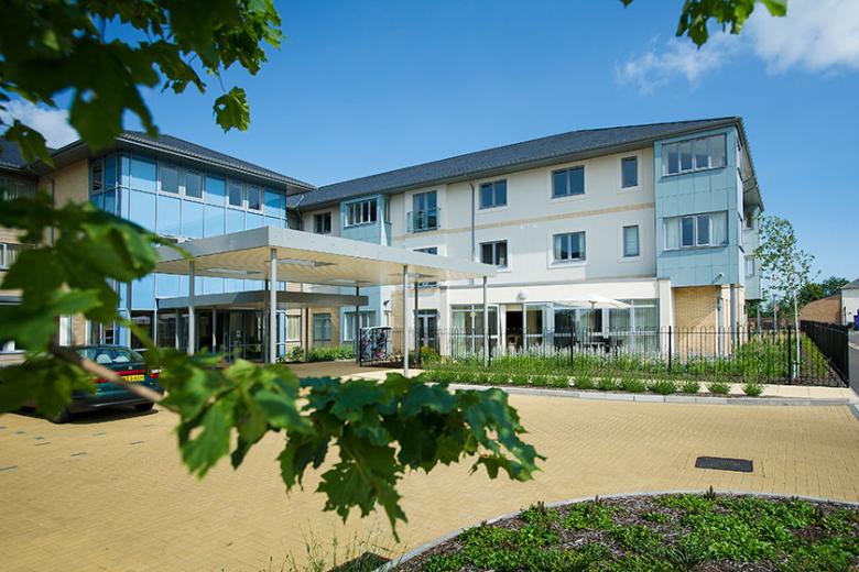 Contemporary, bright retirement living building. The bold blue pops of colour on a selection of the elevations gives a softer approach to the building against the white and grey. A small carpark features at the front of the property.