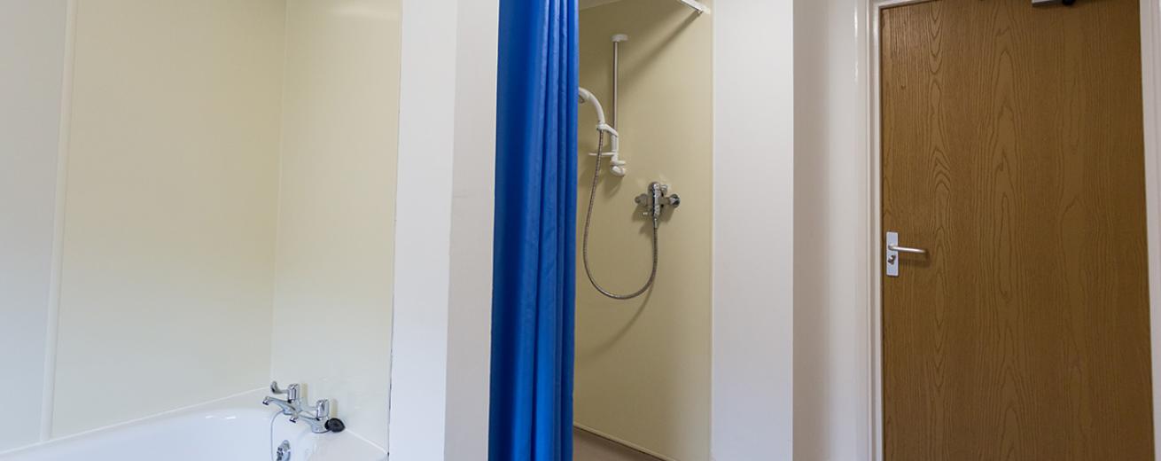 Disability accessible wet room with adjustable shower and blue privacy curtain. As well a bathroom suite.