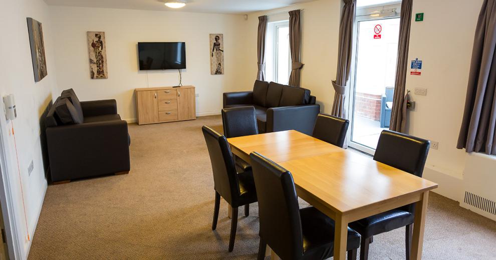 Minimalistic seamless living and dining area with coordinating leather sofa seating and dining chairs, as well as wooden table and television unit. With tonnes of natural light from windows and a door leading out to the patio area.