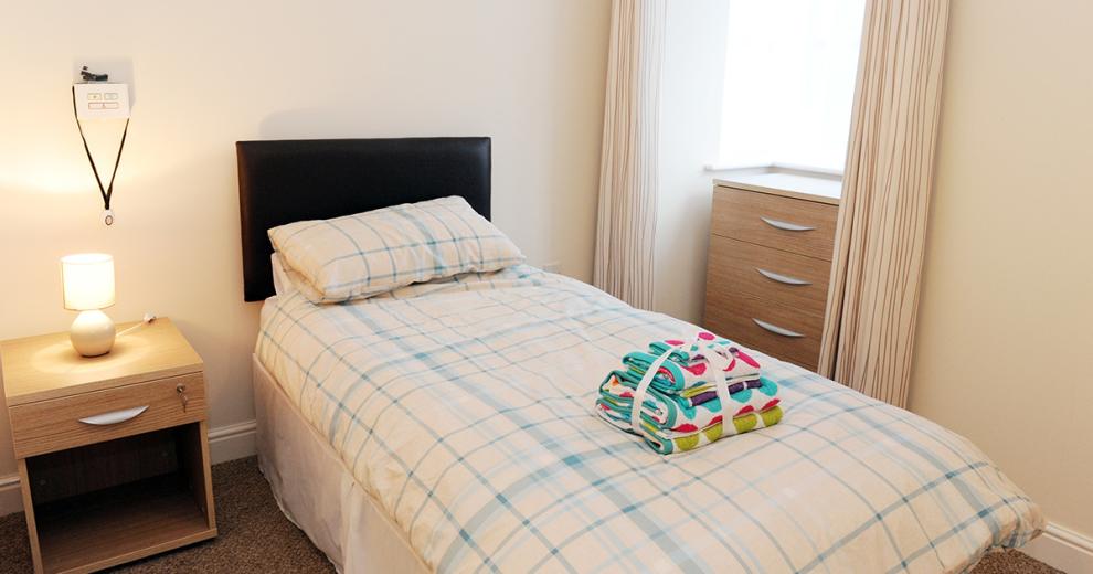 Homely, secure single bedroom with assisted living technology, neutral bedside table and chest of draws which tuck neatly into the window alcove. Presented with fresh linen and bedding.
