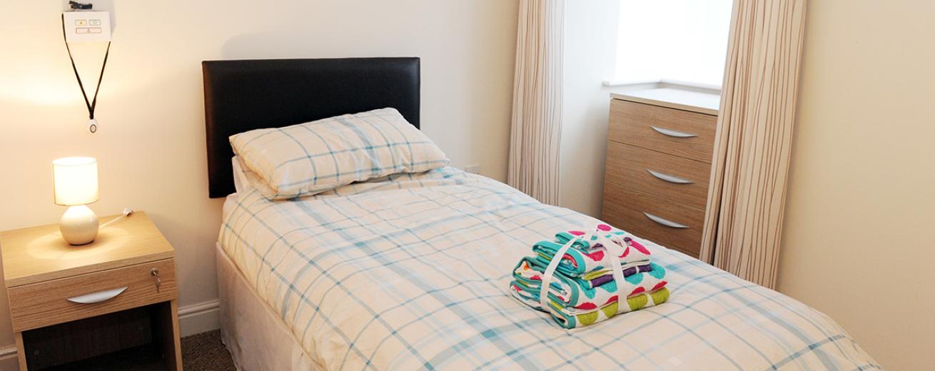 Homely, secure single bedroom with assisted living technology, neutral bedside table and chest of draws which tuck neatly into the window alcove. Presented with fresh linen and bedding.