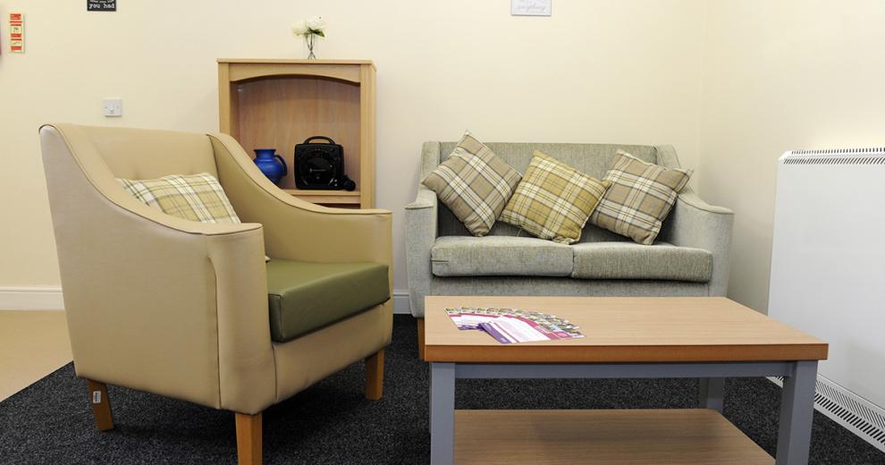 A cosy seating nook consisting of a grey, fabric, double seater sofa and beige leather look armchair with pairing cushions.