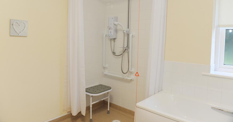 Painted cream and squared white tiled assisted wet room.  Consisting of walk-in and seated shower corner as well as a good sized bathtub.