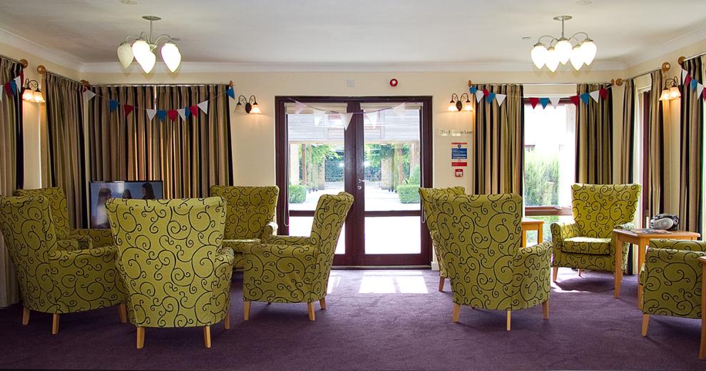A compact seating area with a dark purple carpet to contrast against the multitoned green swirled patterned chesterfield armchairs.