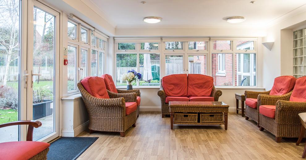 Neutrally styled conservatory room with a wicker furniture set consisting of a two-seater sofa, four arm chairs and coffee table on a natural wooden floor, leading out into a fenced communal garden.