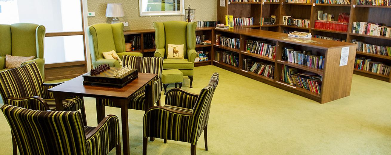 The bold green arm chairs with matching footstools look cosy and inviting in front of the multiple shelving pieces all holding an array of books. The room also hosts four lovely green, grey and black stripped chairs that surround a risen chess board on a squared table.