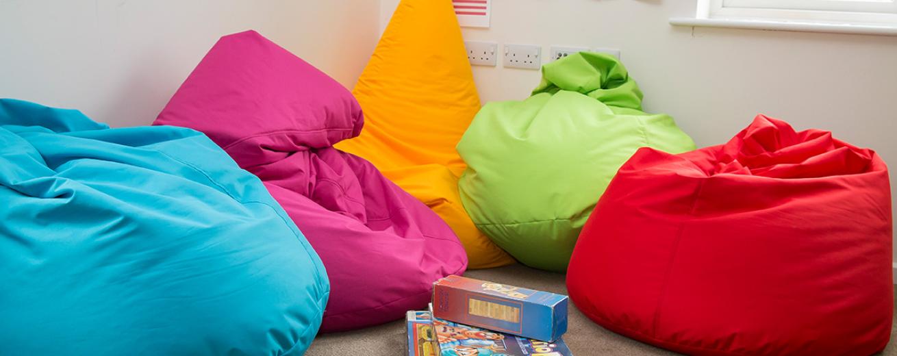 Comfortable, plush, multicoloured, vibrant bean bag seating area within easy reach of a stack of games.